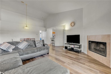 Living room with wood finished floors, high vaulted ceiling, and a tile fireplace