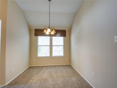 Spare room with a chandelier, carpet flooring, and vaulted ceiling