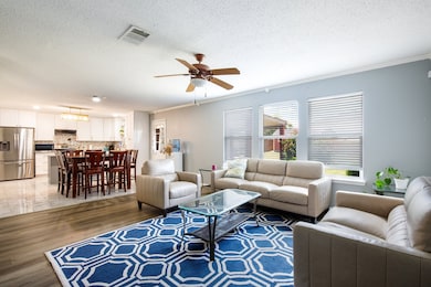 Living room featuring a textured ceiling, light wood-style flooring, a ceiling fan, and crown molding