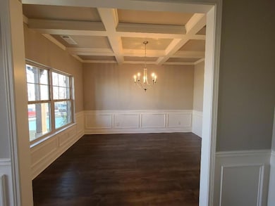 Unfurnished dining area featuring wainscoting, a decorative wall, beam ceiling, coffered ceiling, and ornamental molding