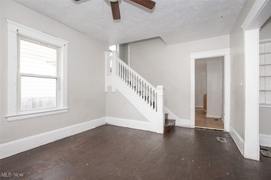Unfurnished living room featuring dark wood finished floors, stairs, a ceiling fan, and a textured ceiling