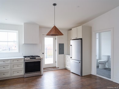 Kitchen featuring appliances with stainless steel finishes, light countertops, dark wood finished floors, electric panel, and pendant lighting