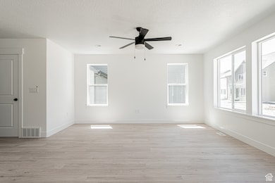 Unfurnished room featuring a textured ceiling, light wood-type flooring, and a ceiling fan