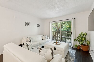 This light-filled living room offers a peaceful view of the tree-lined greenbelt just beyond the sliding doors. The seamless transition to the private balcony creates a relaxing indoor-outdoor flow.