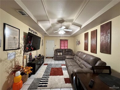Tiled living room featuring ceiling fan, a raised ceiling, and a textured ceiling