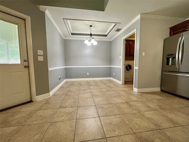 Unfurnished dining area with a tray ceiling, light tile patterned floors, a chandelier, washer / dryer, and crown molding