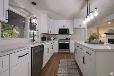 Kitchen featuring white cabinetry, hanging light fixtures, stainless steel appliances, light stone countertops, and dark wood-type flooring