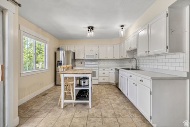 Kitchen with backsplash, appliances with stainless steel finishes, white cabinets, and light tile patterned floors