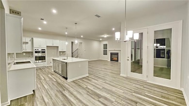 Kitchen with stainless steel appliances, open floor plan, light countertops, white cabinets, and backsplash