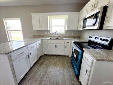 Kitchen with appliances with stainless steel finishes, a peninsula, wood finished floors, white cabinetry, and light stone countertops