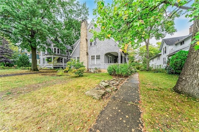 New England style home featuring a stone chimney, shingled siding, covered porch, and front yard