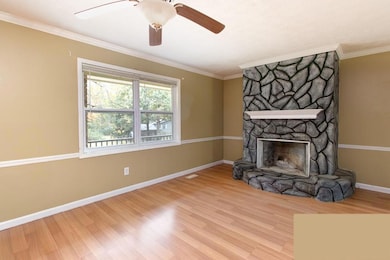 Unfurnished living room featuring wood finished floors, a stone fireplace, crown molding, and ceiling fan