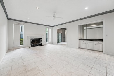 The formal living room boasts a dry bar and a magnificent fireplace, ceiling fan and custom vertical blinds, overlooking a serene patio.