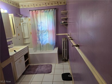 Bathroom with tile patterned flooring, shower / bath combination with curtain, radiator heating unit, and vanity