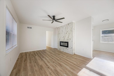 Unfurnished living room featuring light wood-style floors, a ceiling fan, and a high end fireplace