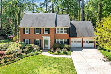 Colonial house featuring concrete driveway, an attached garage, brick siding, and a front lawn
