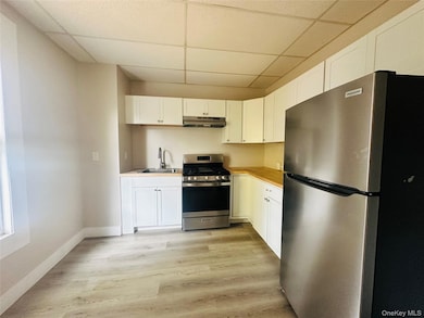 Kitchen featuring appliances with stainless steel finishes, a paneled ceiling, white cabinets, light countertops, and light wood-style flooring