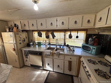 Kitchen featuring white appliances, light countertops, a textured ceiling, light tile patterned floors, and white cabinetry