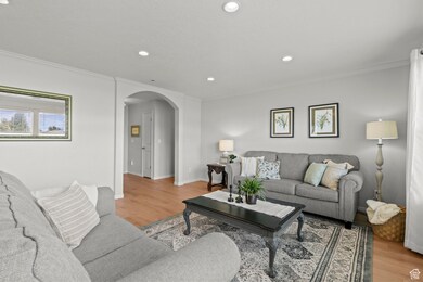 Living room featuring arched walkways, crown molding, light wood-style floors, and recessed lighting