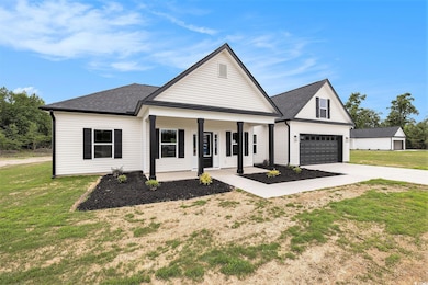 View of front of property with covered porch, driveway, a garage, a front yard, and a shingled roof