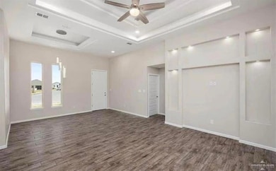 Unfurnished bedroom featuring a raised ceiling, dark wood finished floors, and baseboards