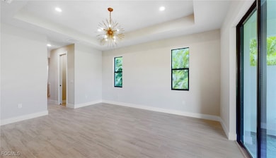 Empty room with a raised ceiling, a chandelier, recessed lighting, and wood finish floors