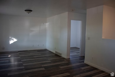 Empty room with dark wood-type flooring and baseboards