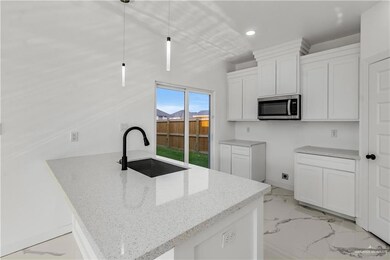 Kitchen with white cabinets, light stone counters, decorative light fixtures, sink, and light tile floors