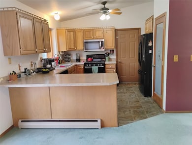 Kitchen featuring black appliances, a baseboard heating unit, light countertops, vaulted ceiling, and a peninsula