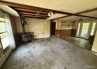 Unfurnished living room featuring a wood stove, wooden walls, and a textured ceiling