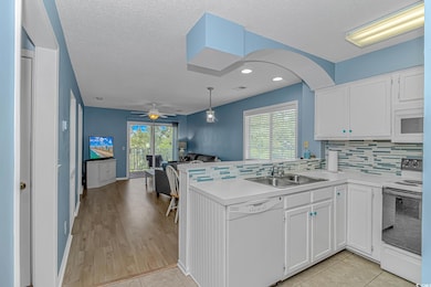 Kitchen with white appliances, open floor plan, white cabinets, decorative backsplash, and light countertops