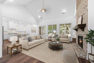 A bright and airy great room with a vaulted ceiling, walls of windows, and a stunning fireplace—designed for relaxation, comfort, and gatherings. Opening to the kitchen, it makes this space perfect for entertaining. This photo has been virtually stag