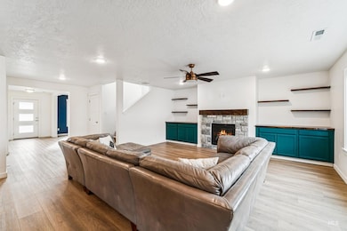 Living area featuring a stone fireplace, light wood-type flooring, a textured ceiling, and a ceiling fan