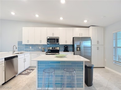 Kitchen featuring backsplash, appliances with stainless steel finishes, white cabinetry, a kitchen bar, and recessed lighting
