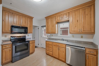 Kitchen with stainless steel appliances, light wood-type flooring, a textured ceiling, brown cabinets, and light countertops