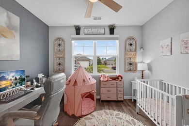 Bedroom with wood finished floors, a nursery area, a ceiling fan, and an office area