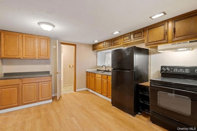 Kitchen featuring black appliances, under cabinet range hood, light wood-style flooring, tasteful backsplash, and brown cabinetry