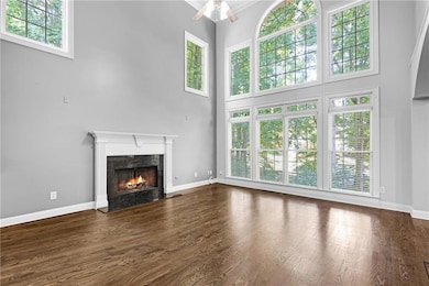 Unfurnished living room with ceiling fan, a fireplace, a high ceiling, and dark wood-type flooring