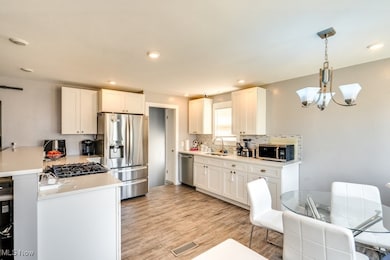 Kitchen featuring light hardwood / wood-style flooring, white cabinets, appliances with stainless steel finishes, decorative light fixtures, and sink