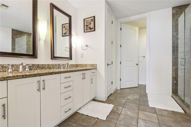 Bathroom with a shower with door, large vanity, tile flooring, and dual sinks
