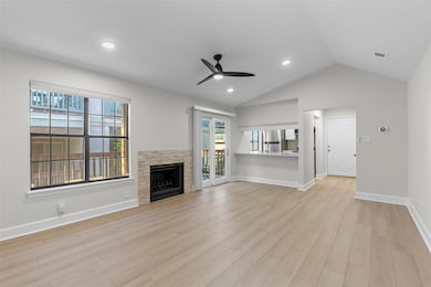 Unfurnished living room with vaulted ceiling, plenty of natural light, a stone fireplace, light wood-style floors, and a ceiling fan