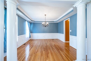 Unfurnished dining area with decorative columns, light wood-type flooring, a tray ceiling, wainscoting, and ornamental molding