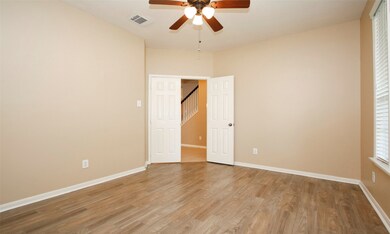 Study with double doors, wood look tile flooring, ceiling fan, entry and staircase visible through an open door.