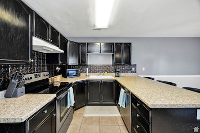 Kitchen with appliances with stainless steel finishes, dark cabinets, and light tile patterned floors