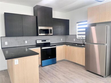 Kitchen with light brown cabinets, sink, light wood-type flooring, tasteful backsplash, and stainless steel appliances