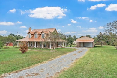 Farmhouse-style home with a front lawn, a chimney, a porch, and an outbuilding