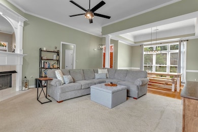 Living area with a tile fireplace, ornamental molding, a raised ceiling, ceiling fan, and decorative columns