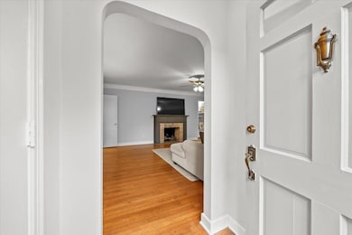 Entrance foyer featuring crown molding, ceiling fan, light wood-type flooring, baseboards, and a fireplace