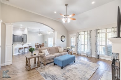 Living room with ceiling fan, ornate columns, arched walkways, light wood-style floors, and recessed lighting