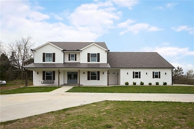 Modern farmhouse featuring concrete driveway, a porch, a front lawn, and metal roof
